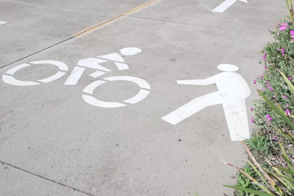 Close-up of white pedestrian and bike symbols painted on concrete path.